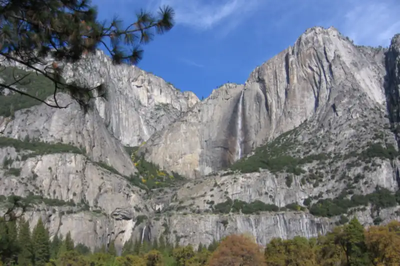 Yosemite Falls and granite cliffs above a valley floor with autumn trees in gold and green