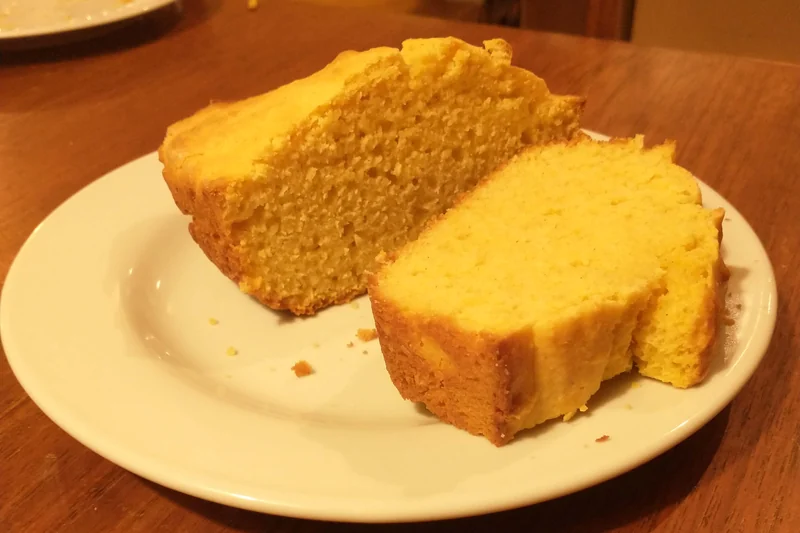 Two thick slices of yellow cornbread on a white plate on a wooden table