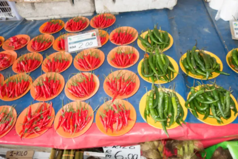 Small plates piled with long red chili peppers and green chili peppers on a market table