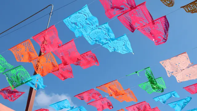 Rows of bright pink, blue, orange and green cut-paper banners strung across a blue sky