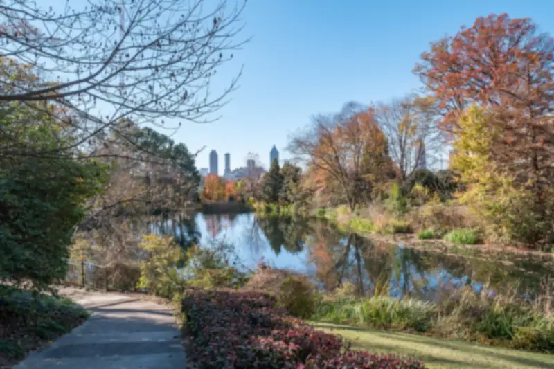 Downtown Atlanta towers in the distance beyond a pond, a path and autumn trees