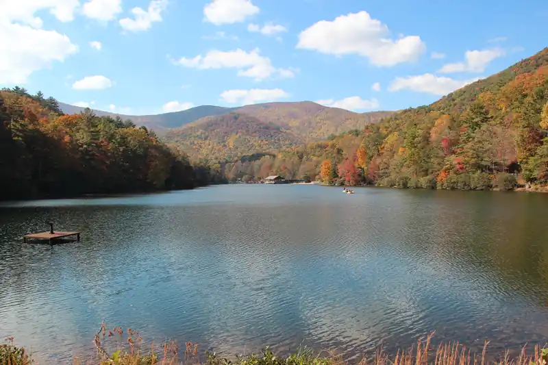 A mountain lake with a small swim dock, surrounded by ridges in orange and red fall color