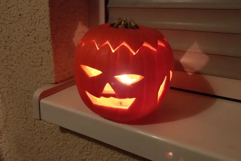A carved pumpkin lit from inside by a candle, sitting on a windowsill