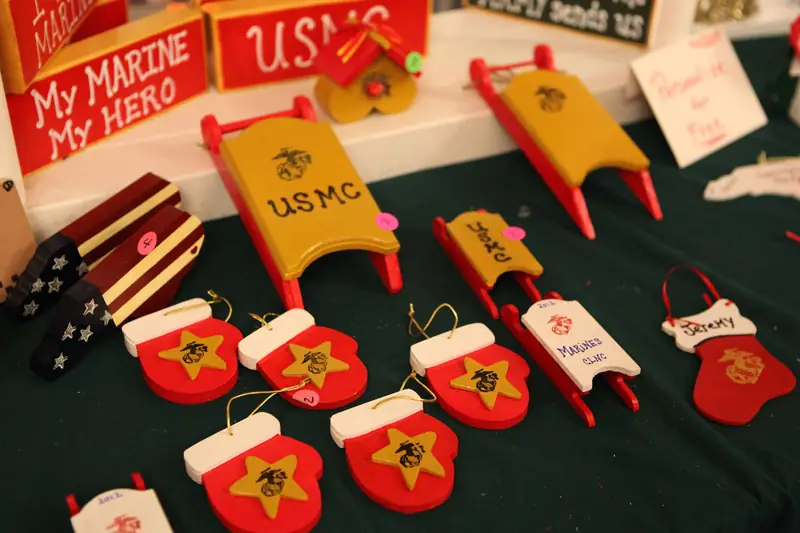 Hand-painted wooden sled and stocking ornaments in red and yellow lined up on a green tablecloth at a craft fair