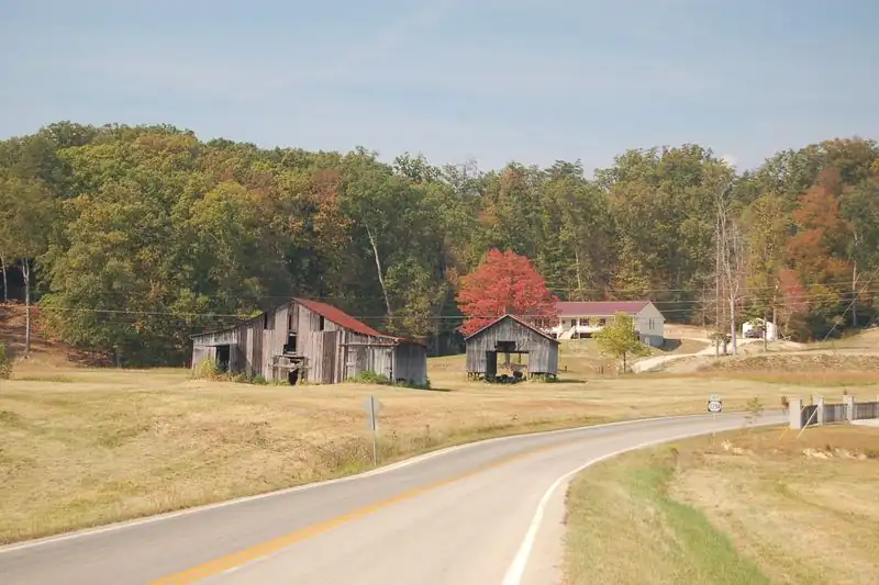 Country road curving past old wooden barns and autumn trees