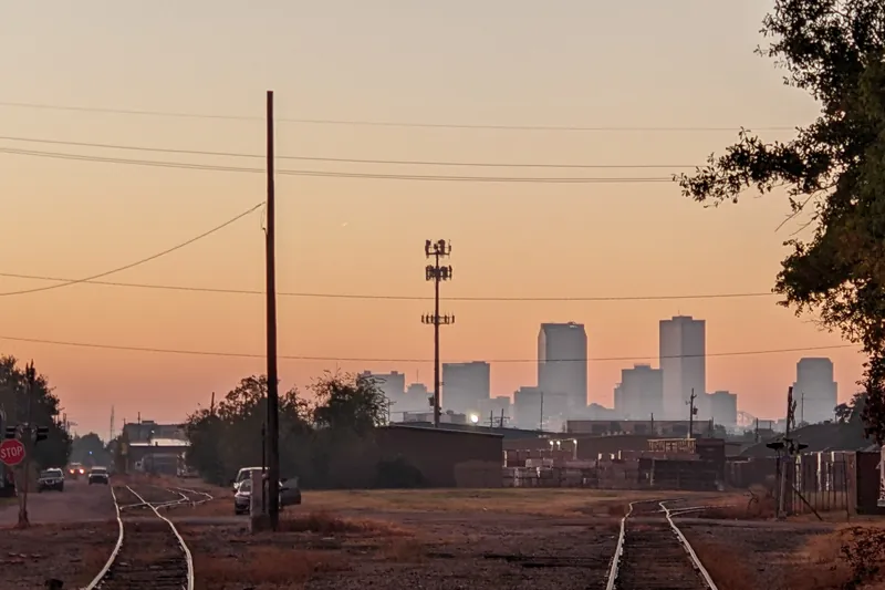 Rail tracks leading toward the New Orleans skyline under an orange sunrise sky