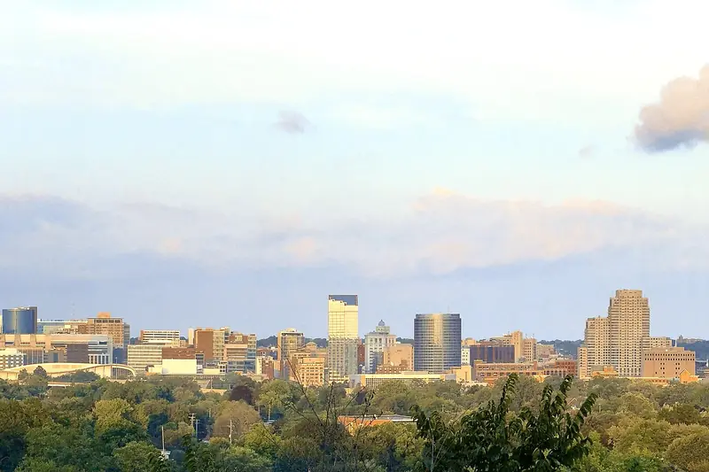 The Grand Rapids skyline along the Grand River under a blue sky with light clouds