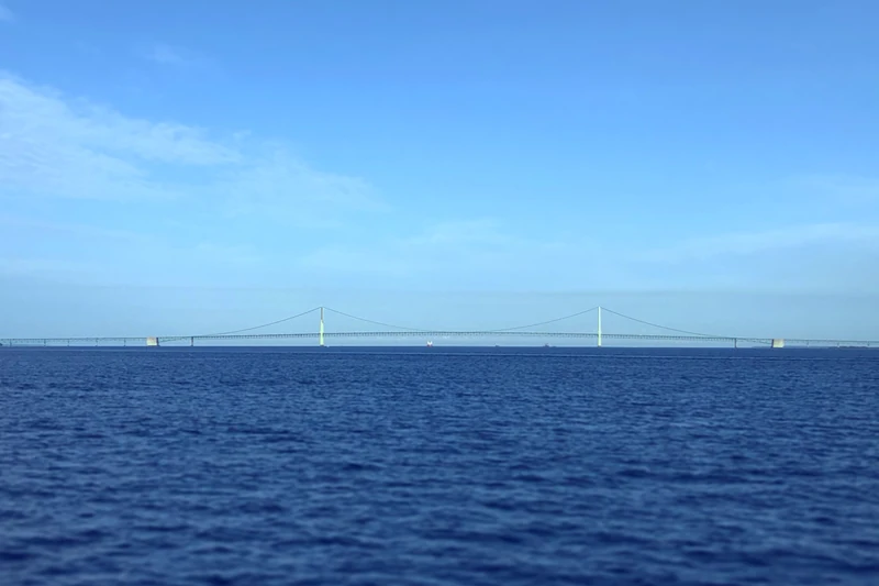 The Mackinac Bridge spanning blue water under a cloudy sky, seen from Lake Huron
