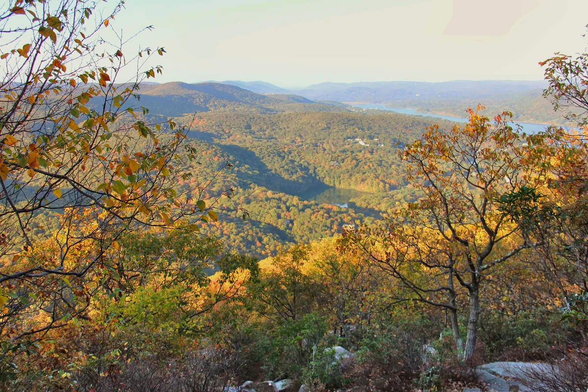 Rocky overlook above orange and yellow fall forests with a pond and distant hills
