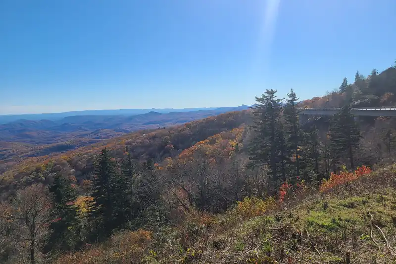 Mountain slopes in orange and rust fall color under a clear blue sky, with an elevated stretch of road on the right