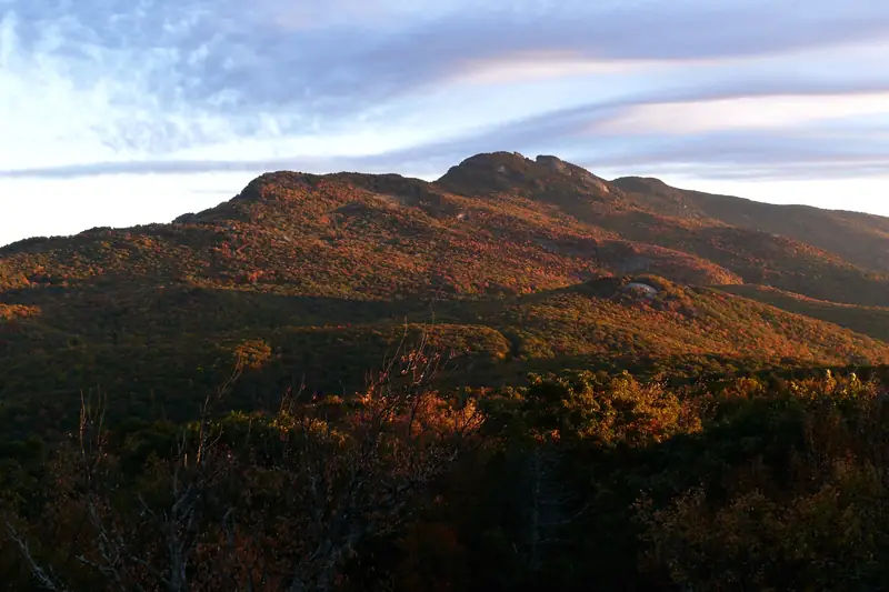 Grandfather Mountain covered in orange and red fall color under a streaky sky
