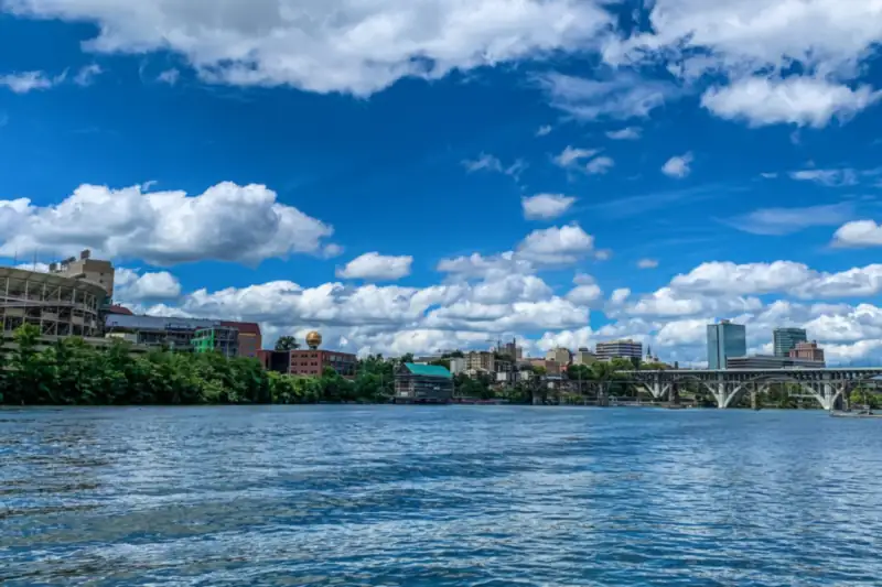 Knoxville downtown towers across a wide river under a clear sky, with wooded hills behind