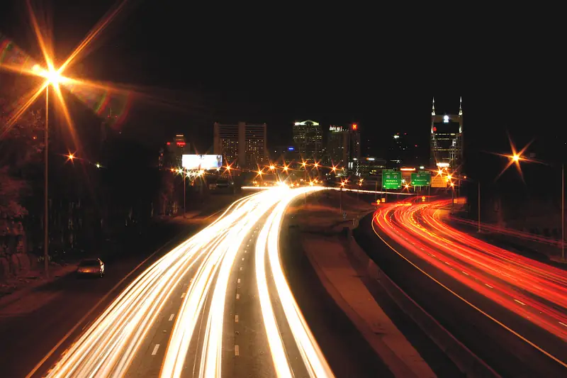 Traffic light trails on an interstate leading toward the lit Nashville skyline at night