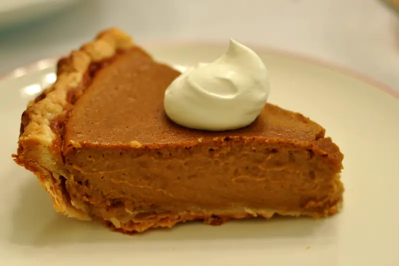 A slice of pumpkin pie topped with whipped cream on a white plate