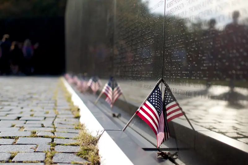 Small American flags standing along the base of the black granite Vietnam Veterans Memorial wall